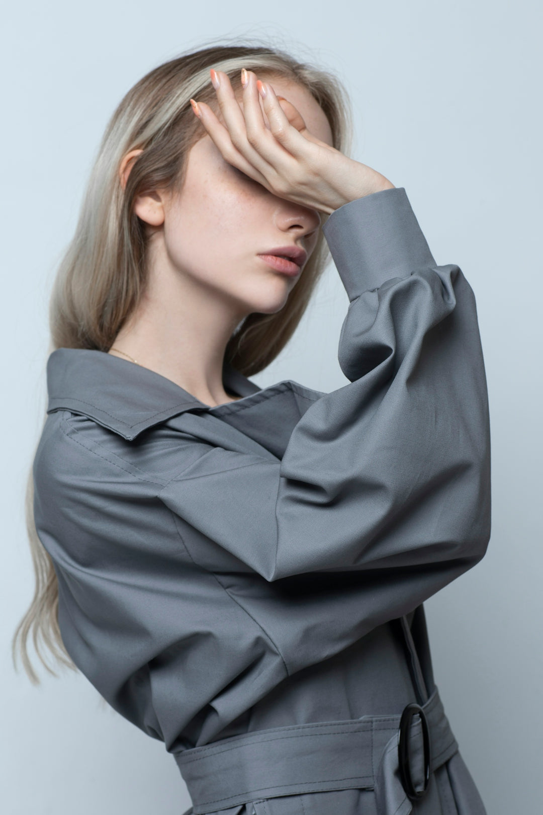A woman with blonde hair wearing a grey trench coat covering her eyes