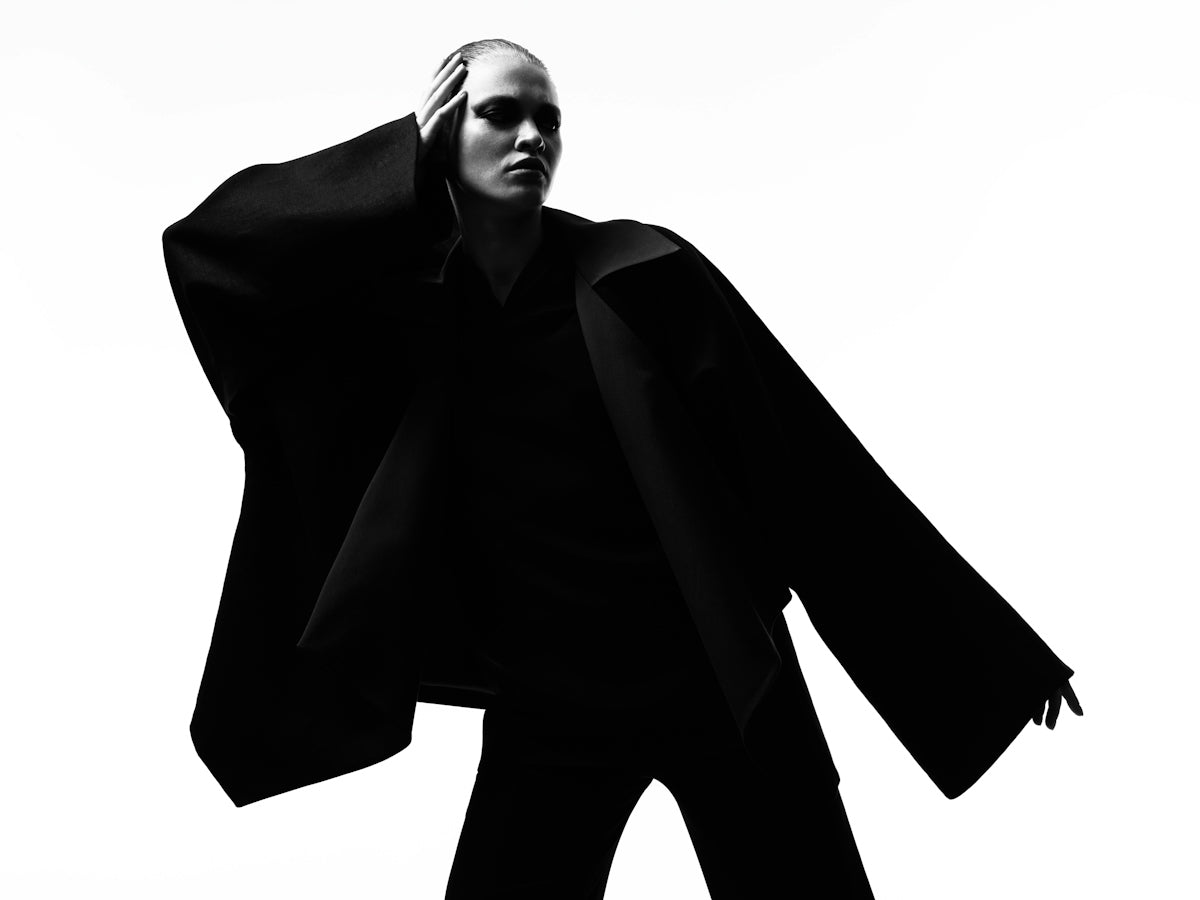 A person in a wide-sleeved black jacket posing in silhouette against a white background
